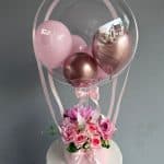 Balon transparent cu baloane roz și cupru, decorat cu flori roz și panglici, perfect pentru petreceri și evenimente speciale.