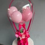 Balon transparent cu baloane roz și flori artificiale, decor elegant pentru evenimente speciale.